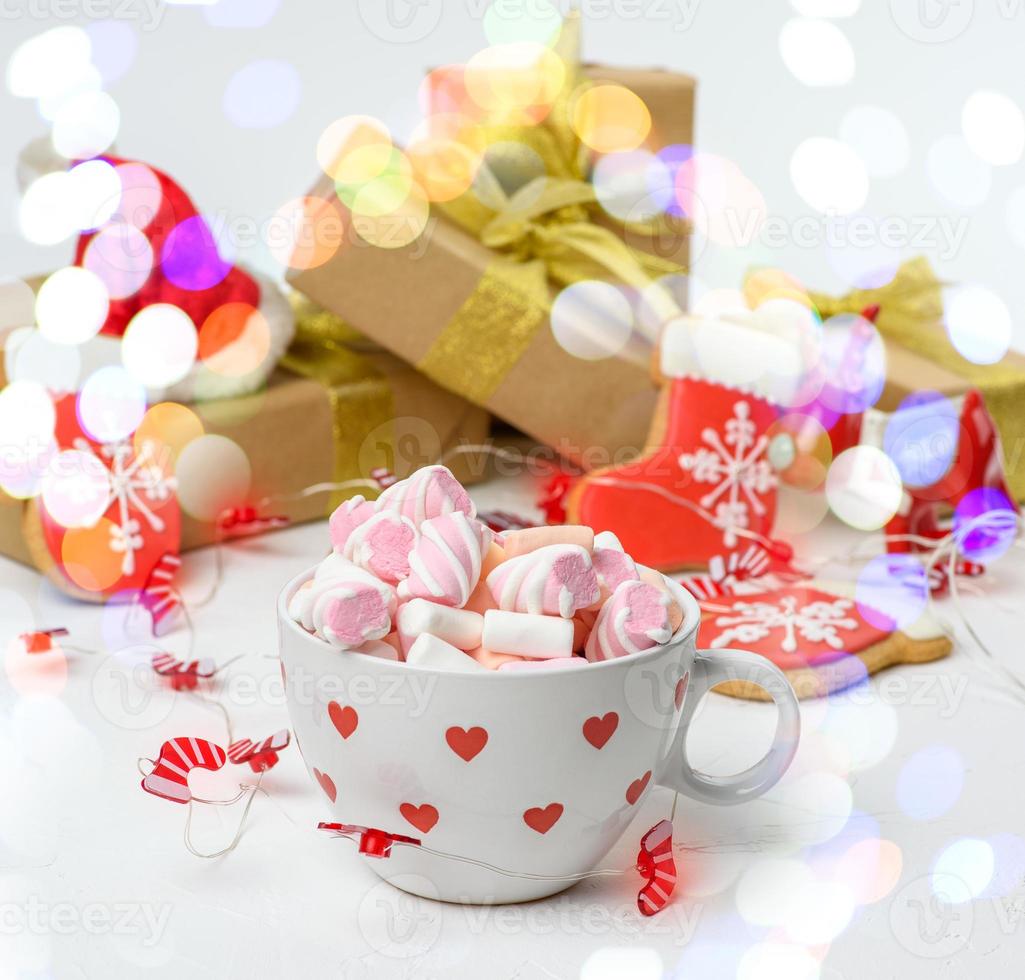 Große Keramiktasse mit Kakao und Marshmallows, dahinter eine Geschenkbox und eine Weihnachtsgirlande foto