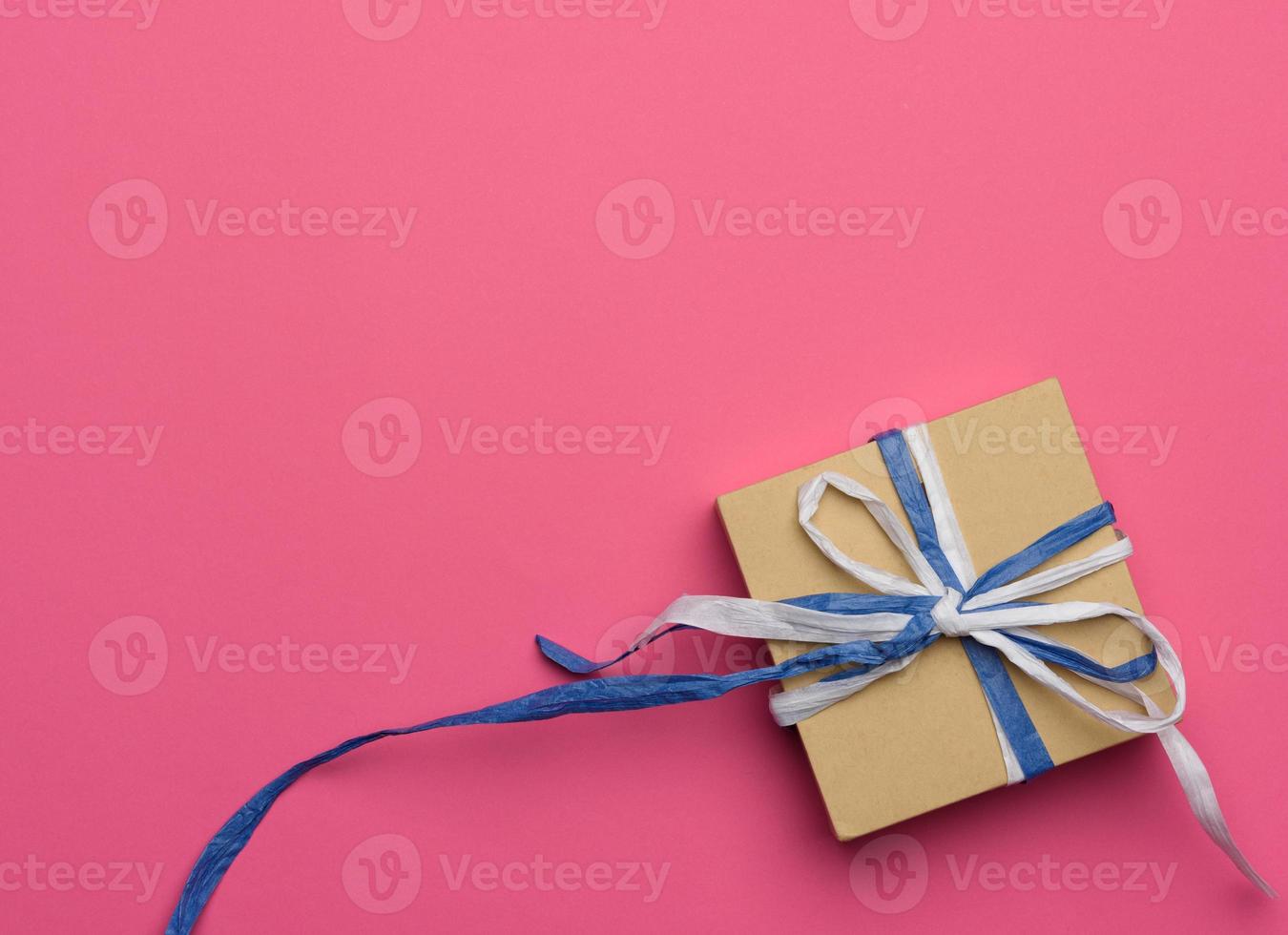 Geschenk verpackt in braunem Kraftpapier auf rosa Hintergrund foto