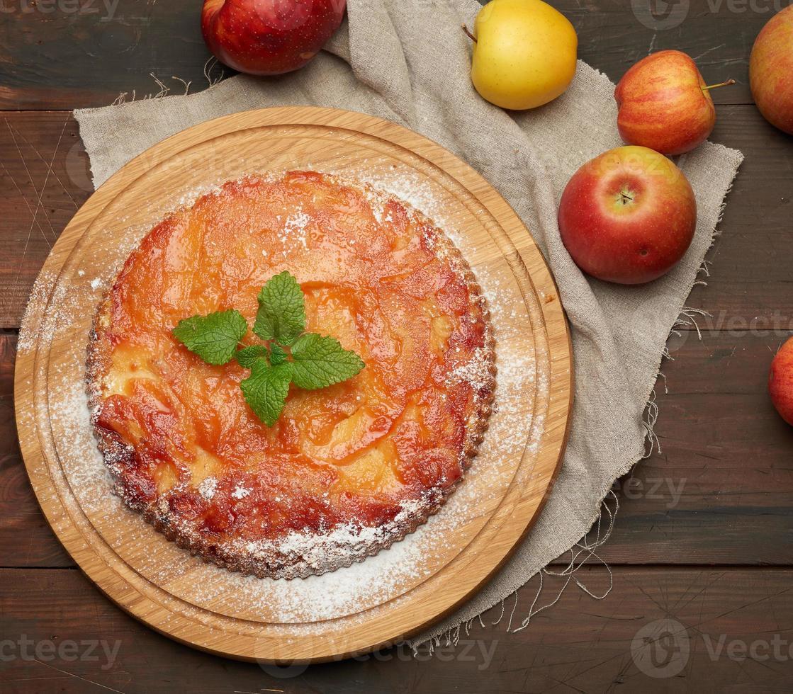 Gebackener runder Apfelkuchen auf Holzbrett und frischen Äpfeln foto
