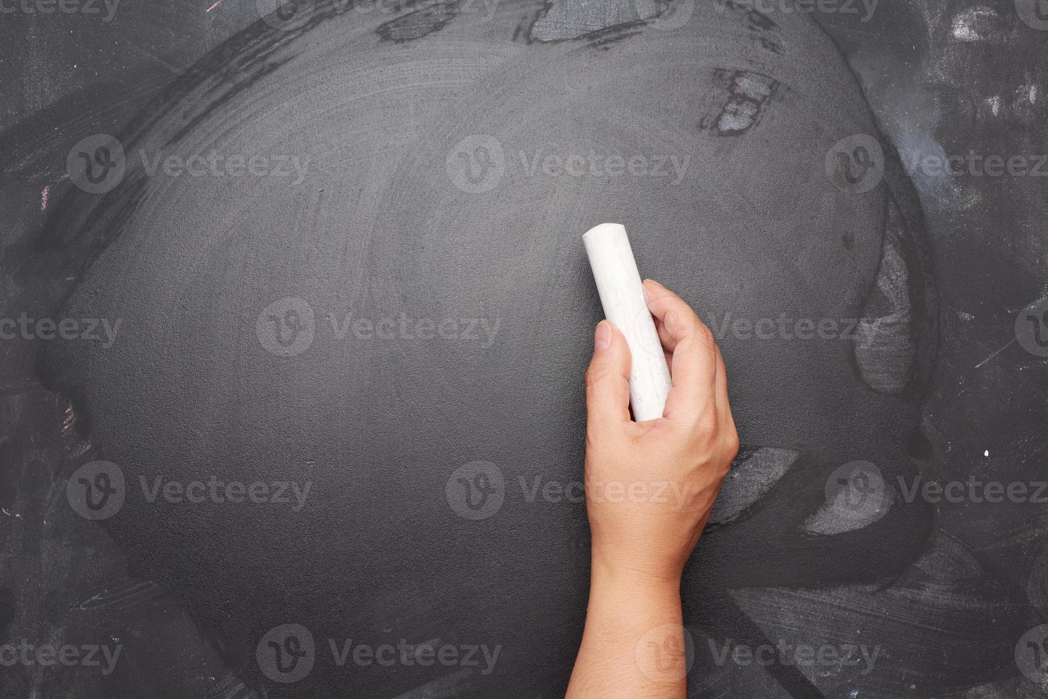 Hand hält ein Stück weiße Kreide auf dem Hintergrund einer leeren schwarzen Kreidetafel, Präsentationskonzept foto