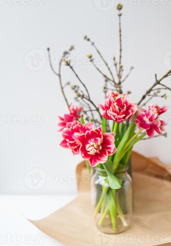 Ein schöner Frühlingsstrauß aus Tulpen steht zusammen mit Frühlingszweigen in einer Vase. überraschungskonzept, geburtstag. vertikales Foto, Platz für eine Inschrift. foto