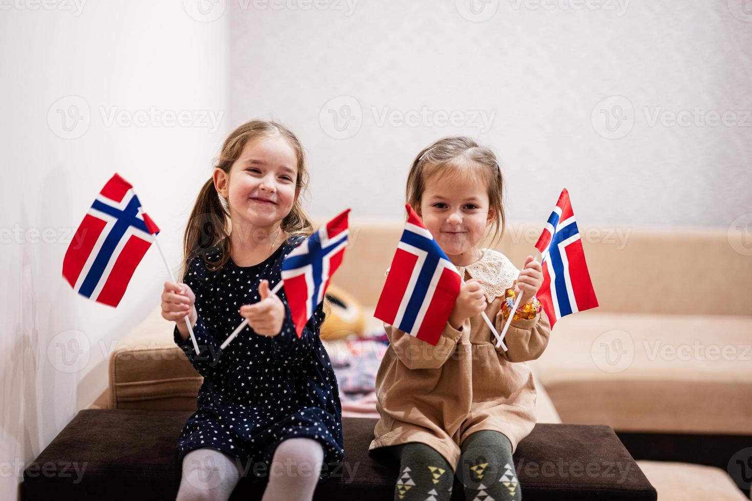 zwei schwestern sitzen zu hause auf einer couch mit norwegischen fahnen an den händen. Norwegen Kinder Mädchen mit Flagge. foto