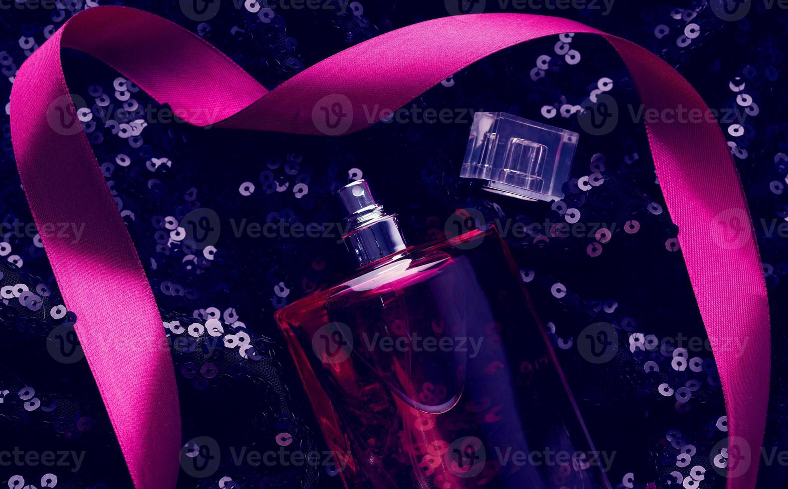 Rosa Glasflasche mit rosa Parfümflüssigkeit auf schwarzem Hintergrund mit glänzenden Pailletten foto