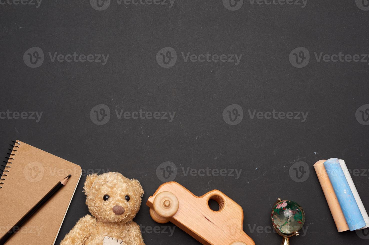 Brauner Teddybär, Holzspielzeugauto und Glaskugel auf schwarzem Kreidebrett, zurück zur Schule foto