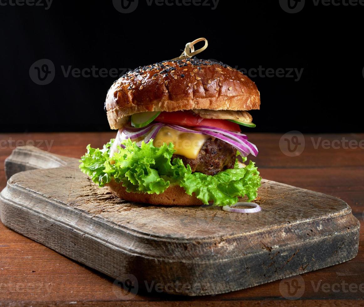 Leckere Burger mit gebratenem Rinderkotelett, Tomate, Salat und Zwiebeln, knuspriges Weißmehlbrötchen mit Sesam foto