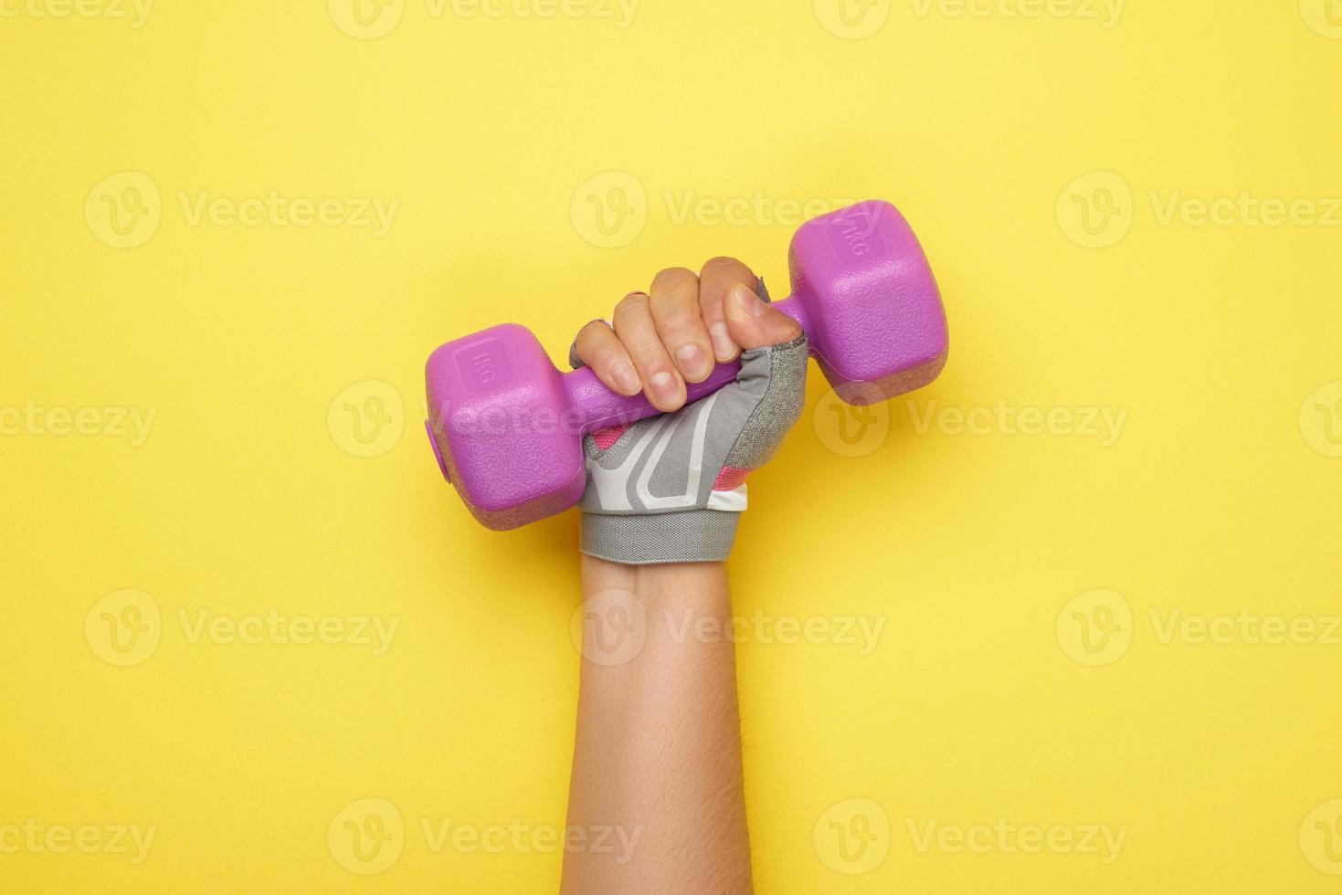 weibliche hand in einem rosafarbenen sporthandschuh hält eine violette ein-kg-hantel foto