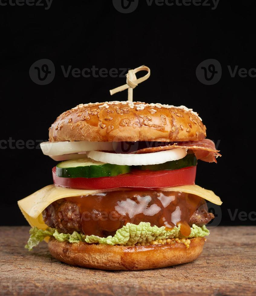 Cheeseburger mit Tomaten, Zwiebeln, Grillkotelett und Sesambrötchen auf einem alten Holzschneidebrett foto