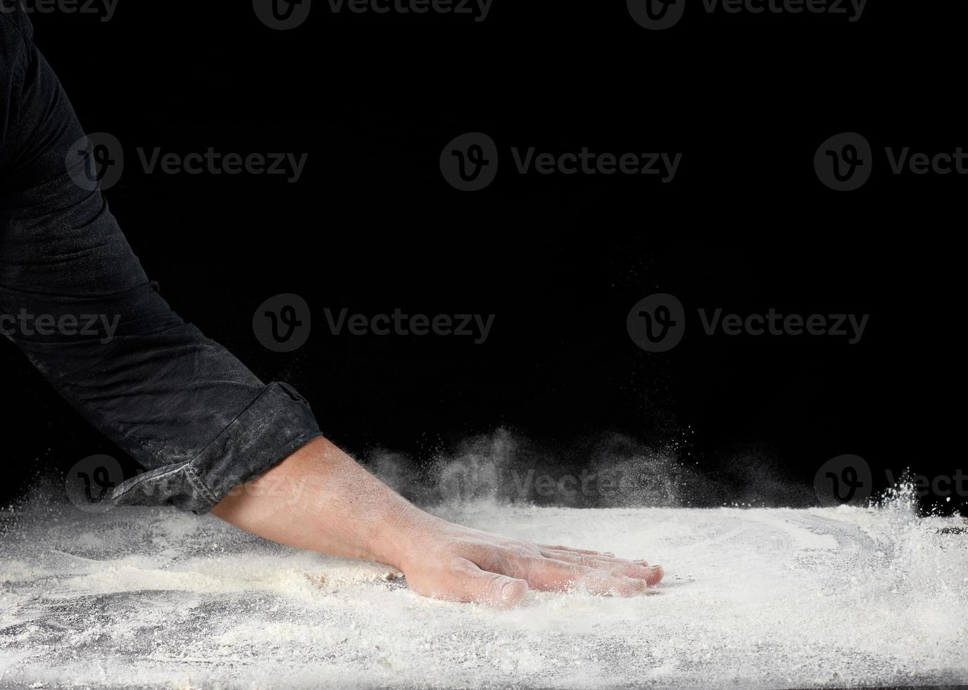Koch in schwarzer Uniform streut weißes Weizenmehl in verschiedene Richtungen foto