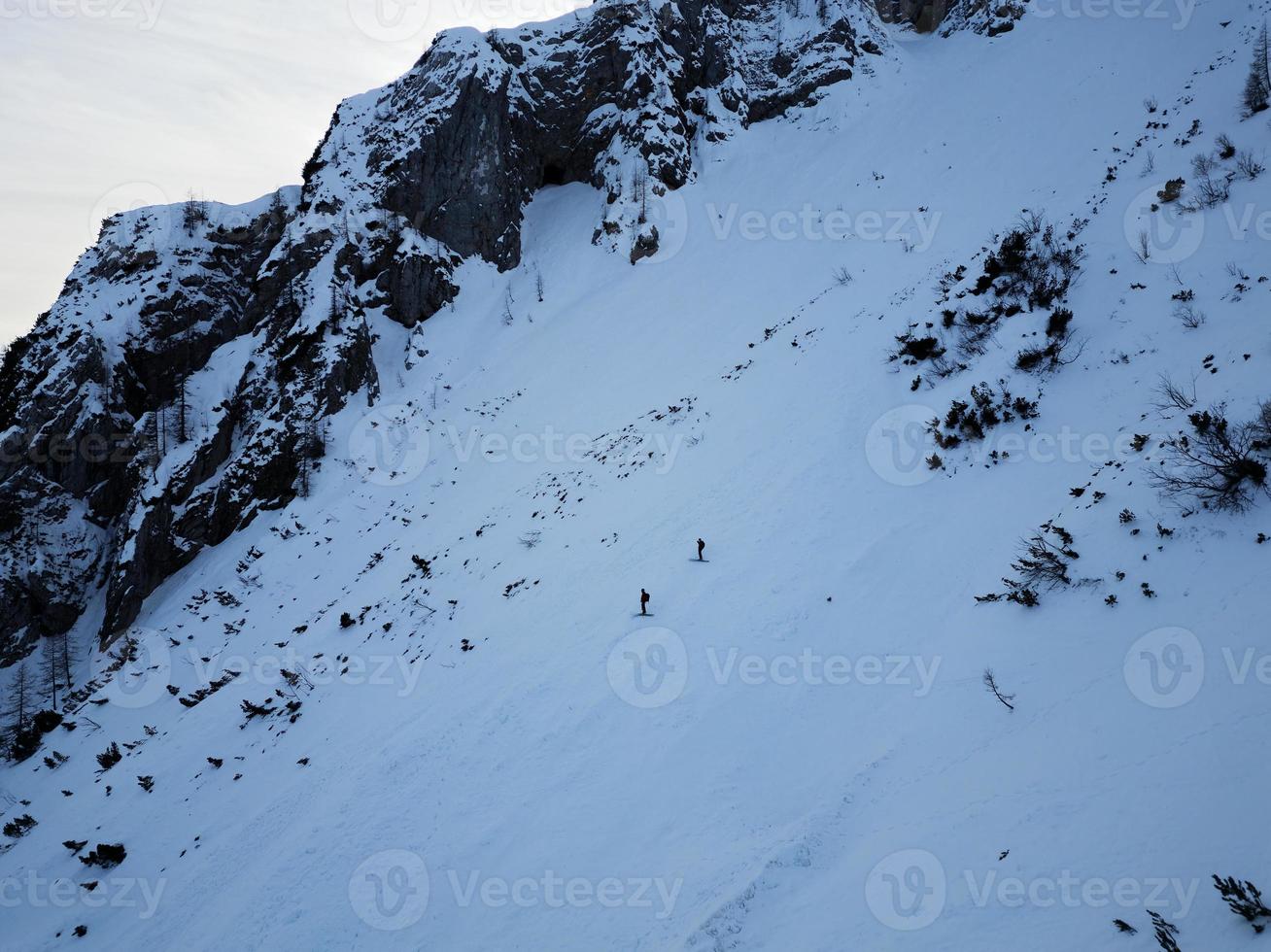 Luftdrohnenansicht von zwei Skifahrern, die im Triglav-Nationalpark den Berg hinunterfahren. Julische Alpen in Slowenien. Adrenalinsport und Winteraktivitäten. Backcountry-Skifahren oder alpines Skifahren. foto