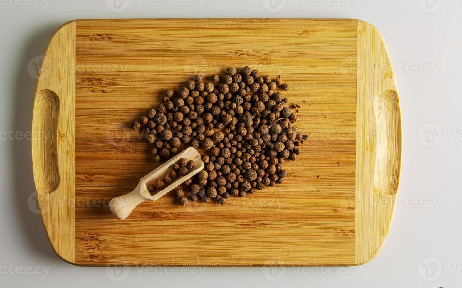 Piment-Erbsen würzen. aromatisches Gewürz für Lebensmittel. Hintergrund getrockneter Samen Pimenterbsen auf einem hölzernen Küchenbrett mit einem Messlöffel. foto