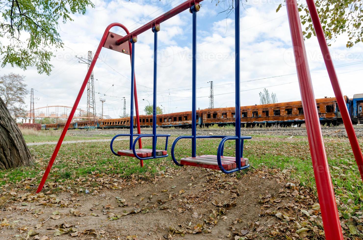 leere schaukeln auf einem leeren spielplatz ohne menschen vor dem hintergrund verbrannter züge in der ukraine foto