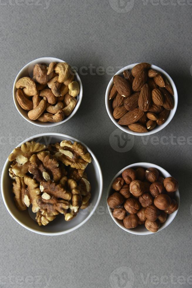 eine Reihe von Nüssen in weißen Tassen auf schwarzem Hintergrund. Erdnüsse, Haselnüsse und Mandeln. Nussbaum. ein köstliches Set von Nüssen. foto