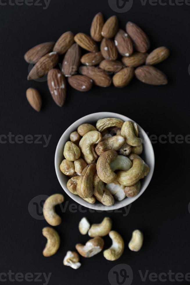 eine Reihe von Nüssen in weißen Tassen auf schwarzem Hintergrund. Erdnüsse, Haselnüsse und Mandeln. Nussbaum. ein köstliches Set von Nüssen. foto
