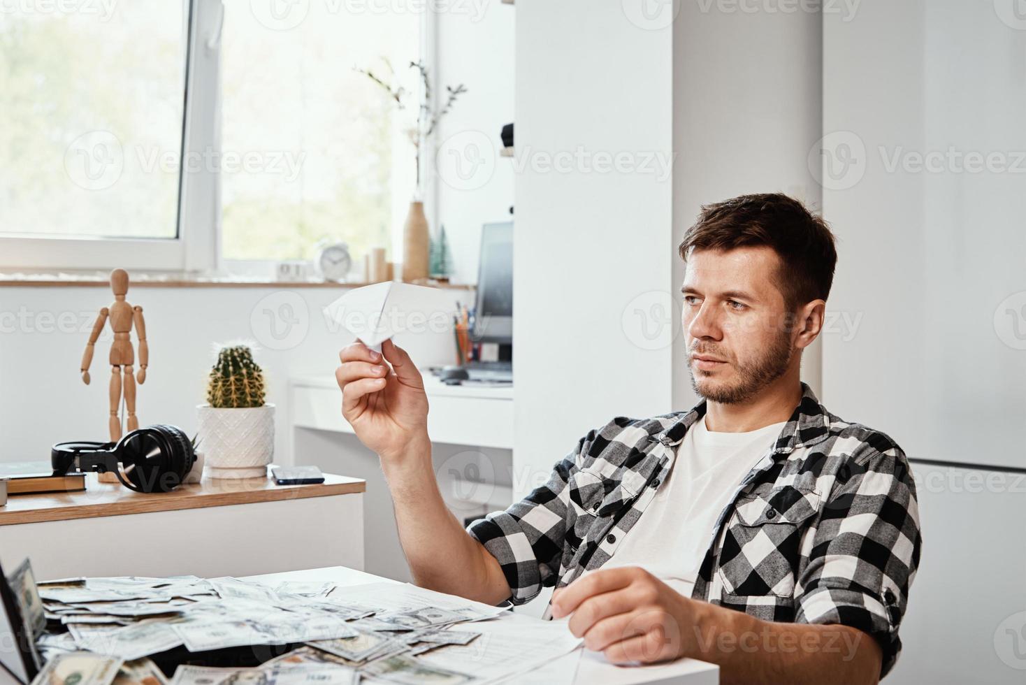 Mann mit Laptop und Dollarscheinen spielt mit Papierebene foto