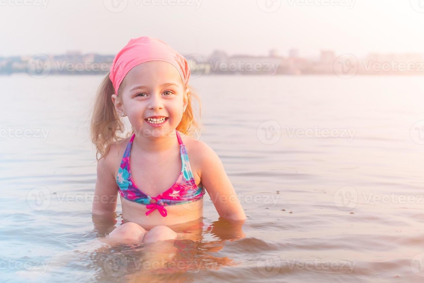 Ein kleines Mädchen badet im Fluss in der Stadt. ein Kind in einem Badeanzug im Wasser im Sommer. foto