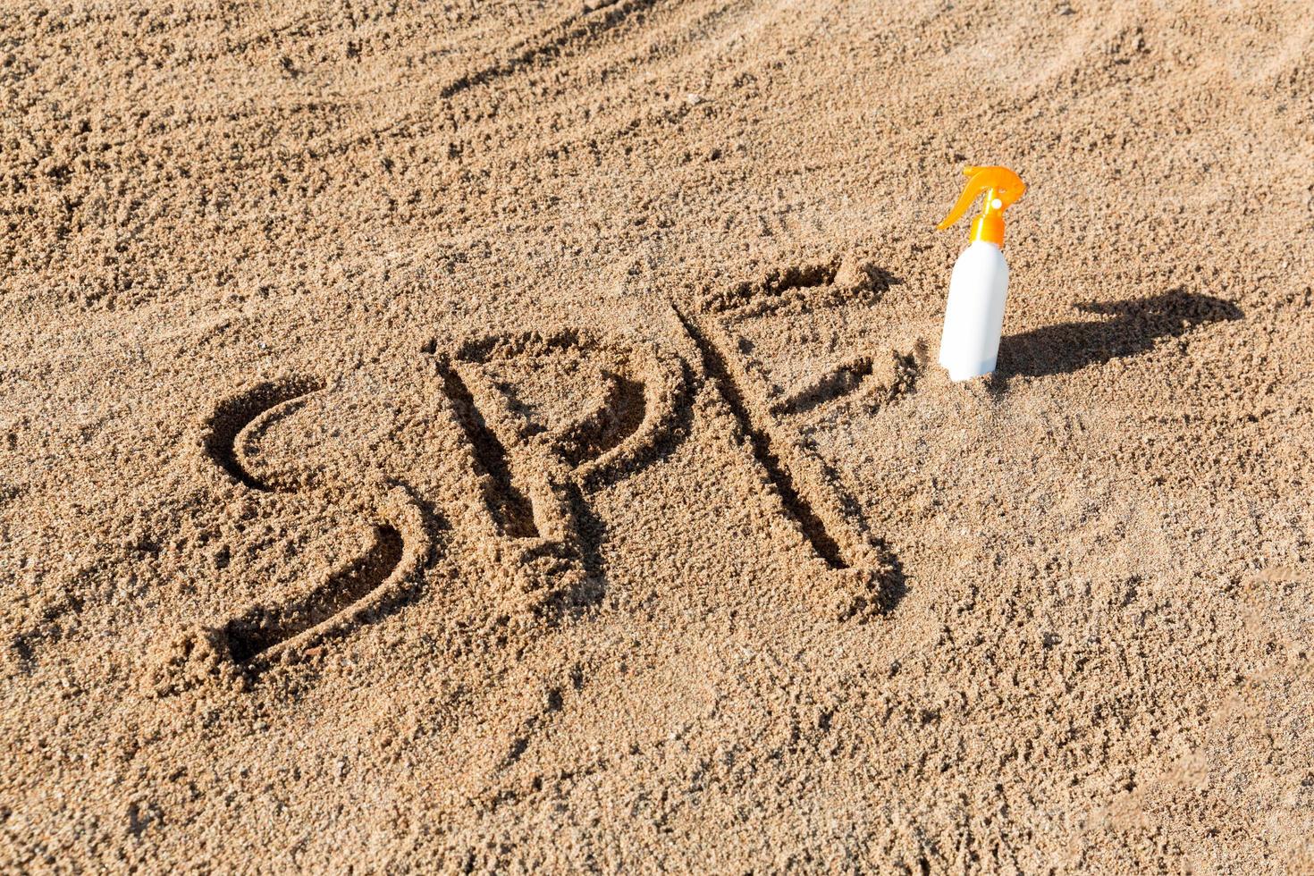 Lichtschutzfaktor. spf-wort geschrieben auf den sand und die weiße flasche mit sonnencreme. hintergrund des hautpflegekonzepts foto