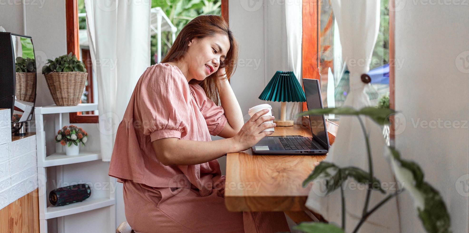 eine glückliche frau in einem café mit einem laptop in der hand und einer papptasse kaffee. Junge weiße Frau mit langen Haaren, die in einem Café sitzt und an ihrem Laptop arbeitet. foto