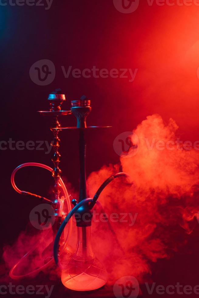 moderne shisha, shisha auf einem rauchigen schwarzen hintergrund mit farbiger beleuchtung und rauch foto