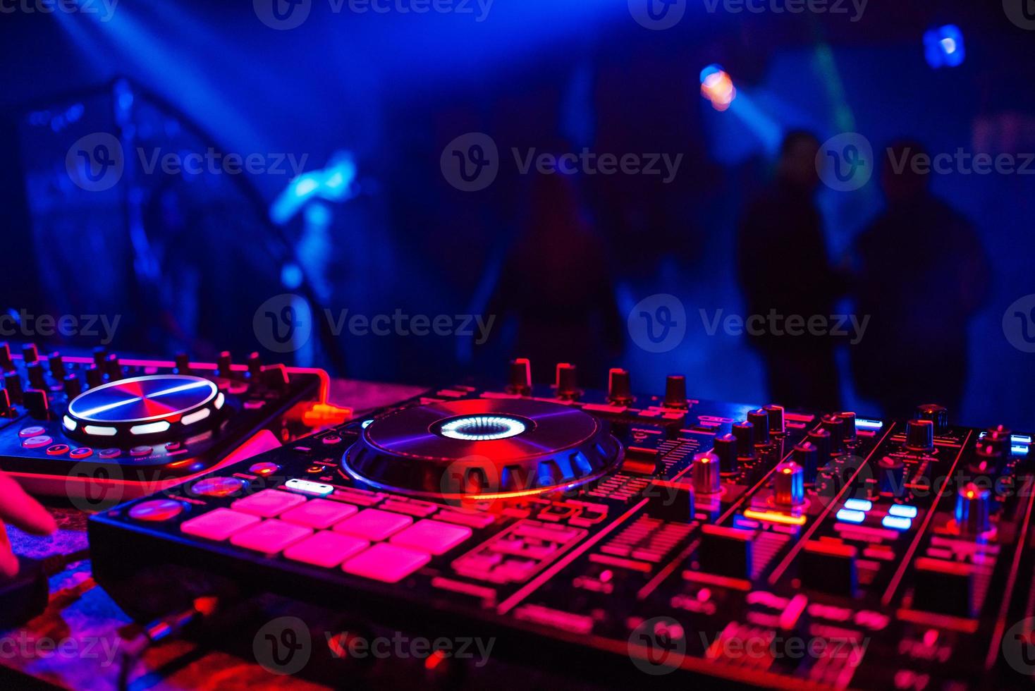 DJ-Konsole zum Mischen von Musik mit verschwommenen Leuten, die auf einer Nachtclubparty tanzen foto