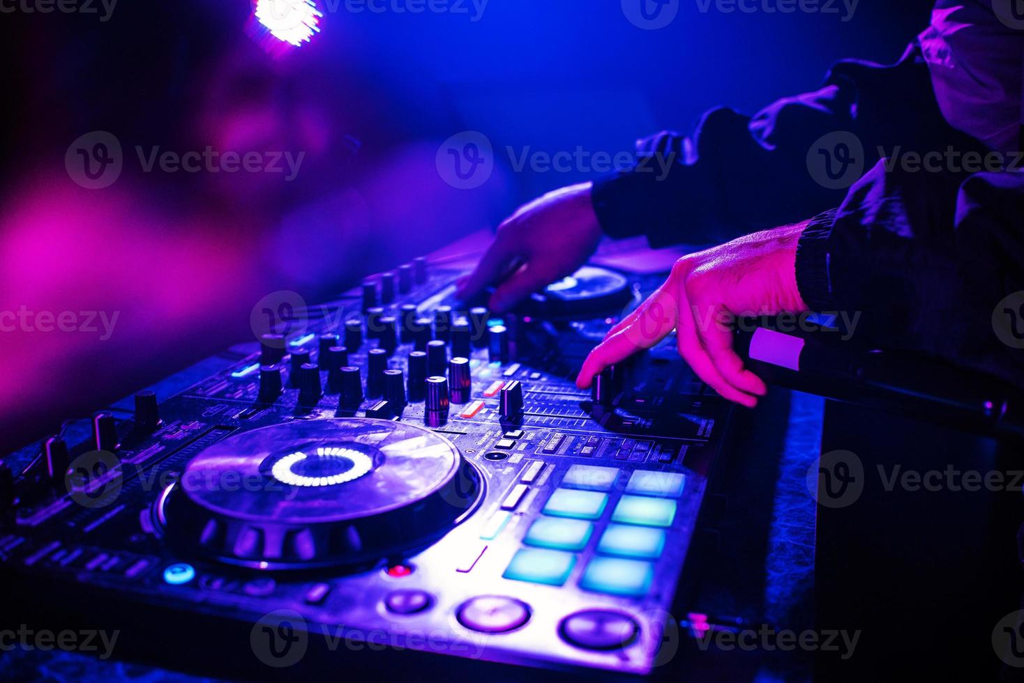 dj-konsole zum mischen von musik mit den händen und mit verschwommenen menschen, die auf einer nachtclubparty tanzen foto