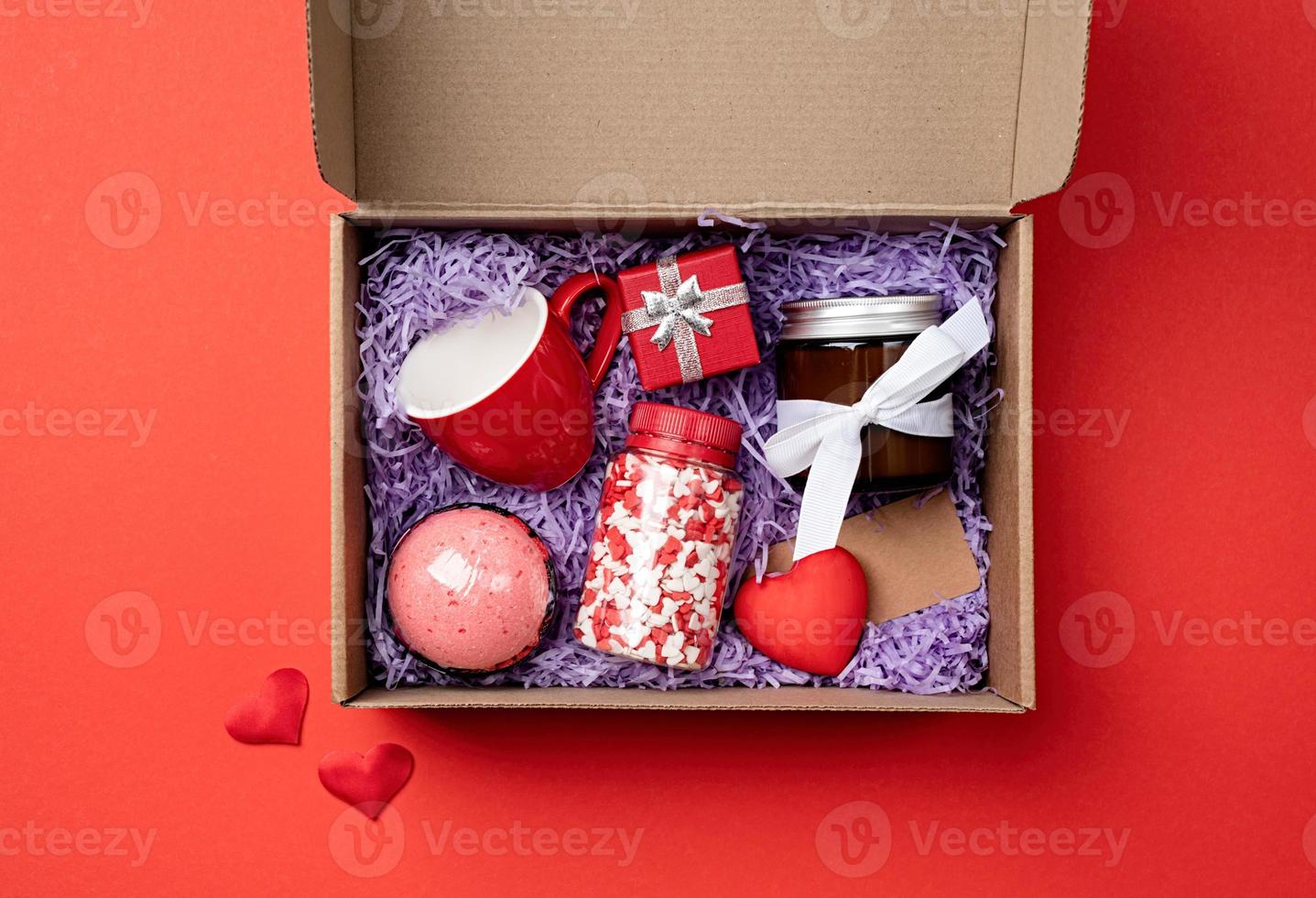saisonale geschenkbox zum valentinstag mit kerze, roter tasse und herzförmigen süßigkeiten auf rotem hintergrund foto