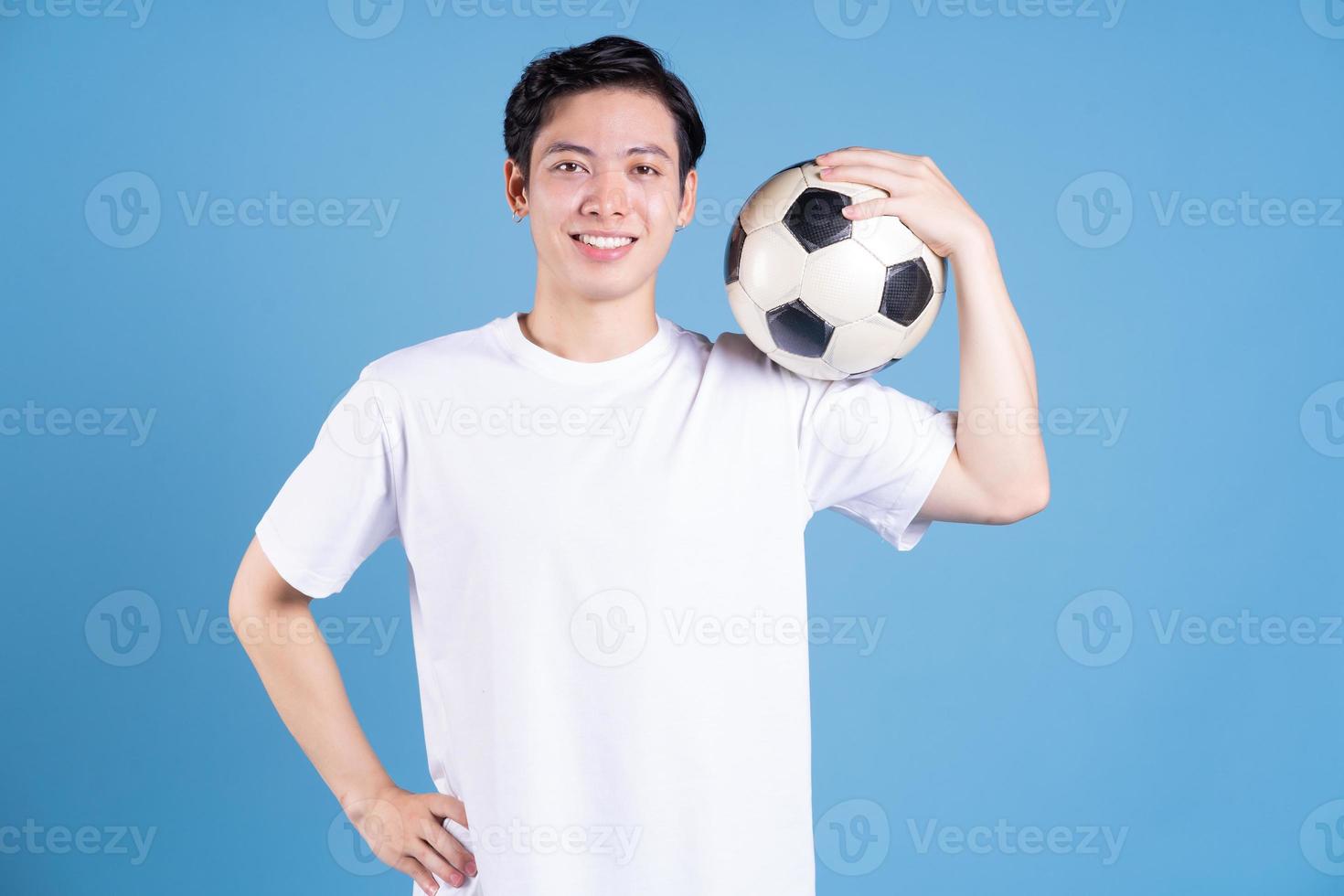 junger asiatischer mann, der ball auf hintergrund hält foto