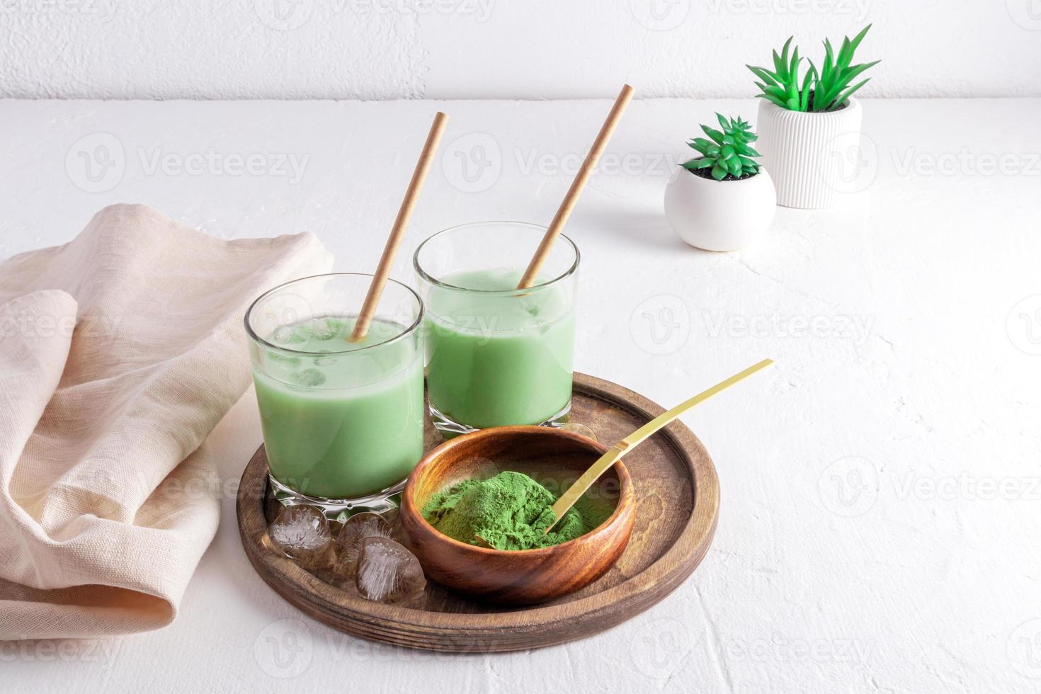 Frisch zubereiteter Matcha-Latte-Tee mit Eiswürfeln auf einem Holztablett und einer Schüssel mit grünem Matcha-Pulver zum Kochen. weißer Hintergrund. Entgiftung. foto