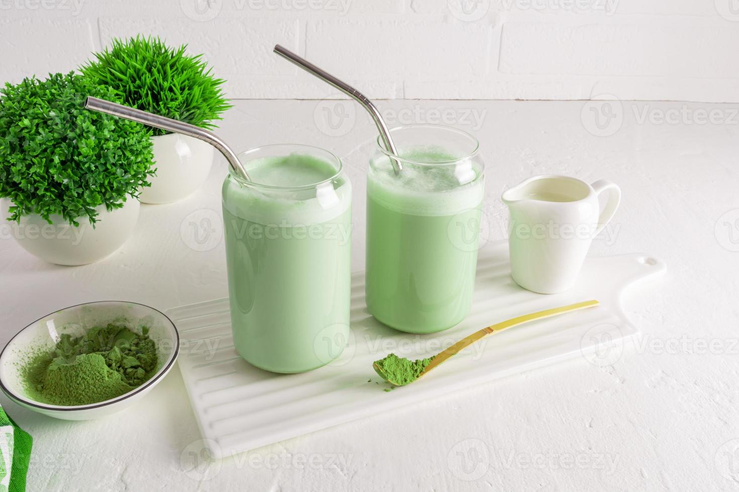 zwei Tassen in Form einer Bierdose mit frisch zubereitetem Matcha-Latte-Tee auf einer weißen Keramikplatte gegenüber der Ziegelwand und Pflanzen in Blumentöpfen. foto