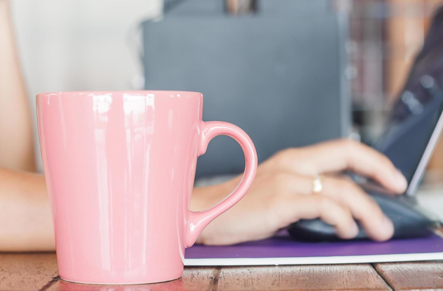 rosa Kaffeetasse mit einer Person, die an einem Laptop arbeitet foto