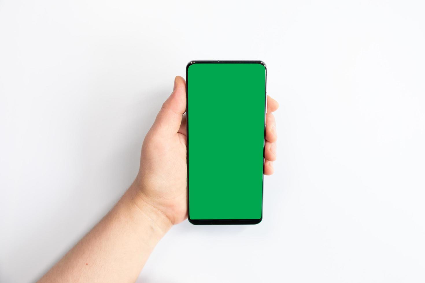Frau, die ein grünes Bildschirmhandy mit einem weißen Hintergrund hält foto