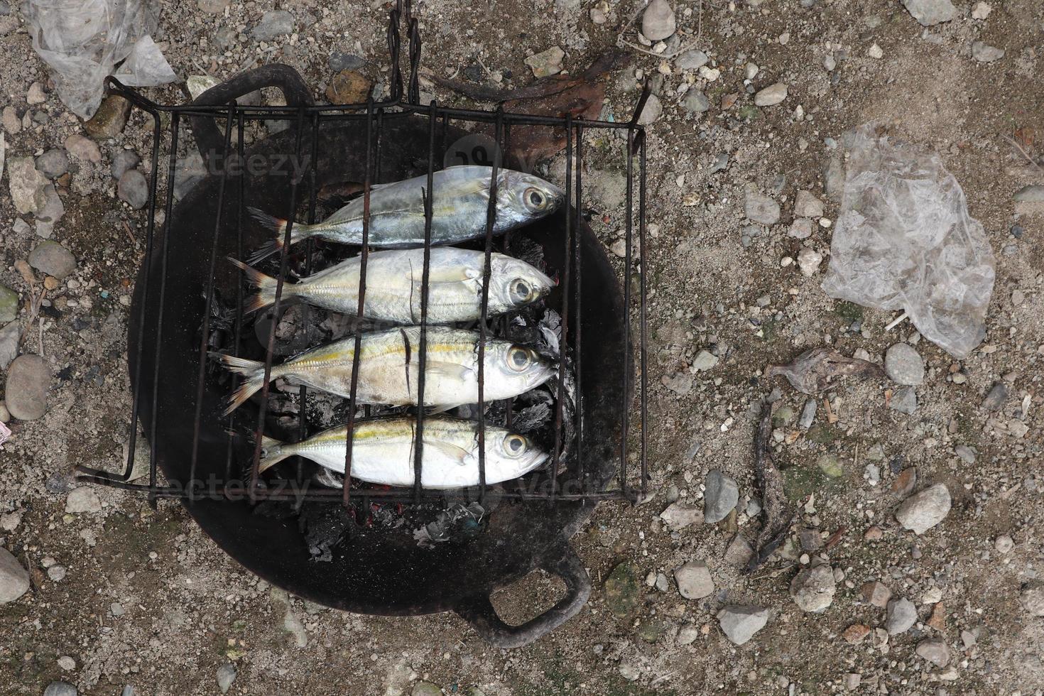 der Prozess der Herstellung von gegrilltem Fisch, der über Kokosnussschalenkohlen verbrannt wird foto