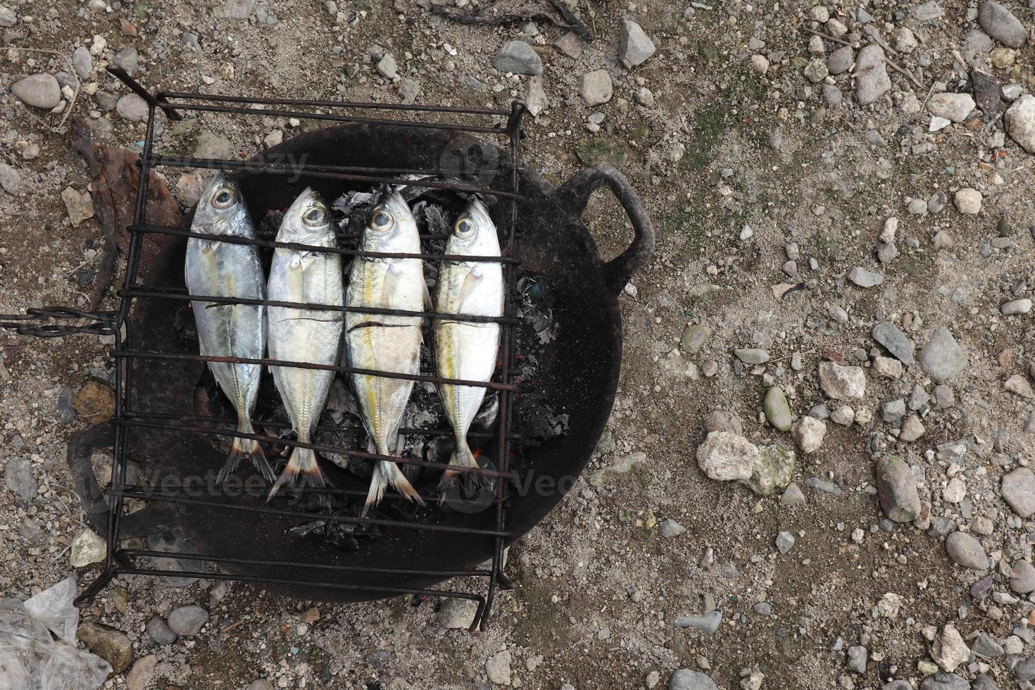 der Prozess der Herstellung von gegrilltem Fisch, der über Kokosnussschalenkohlen verbrannt wird foto