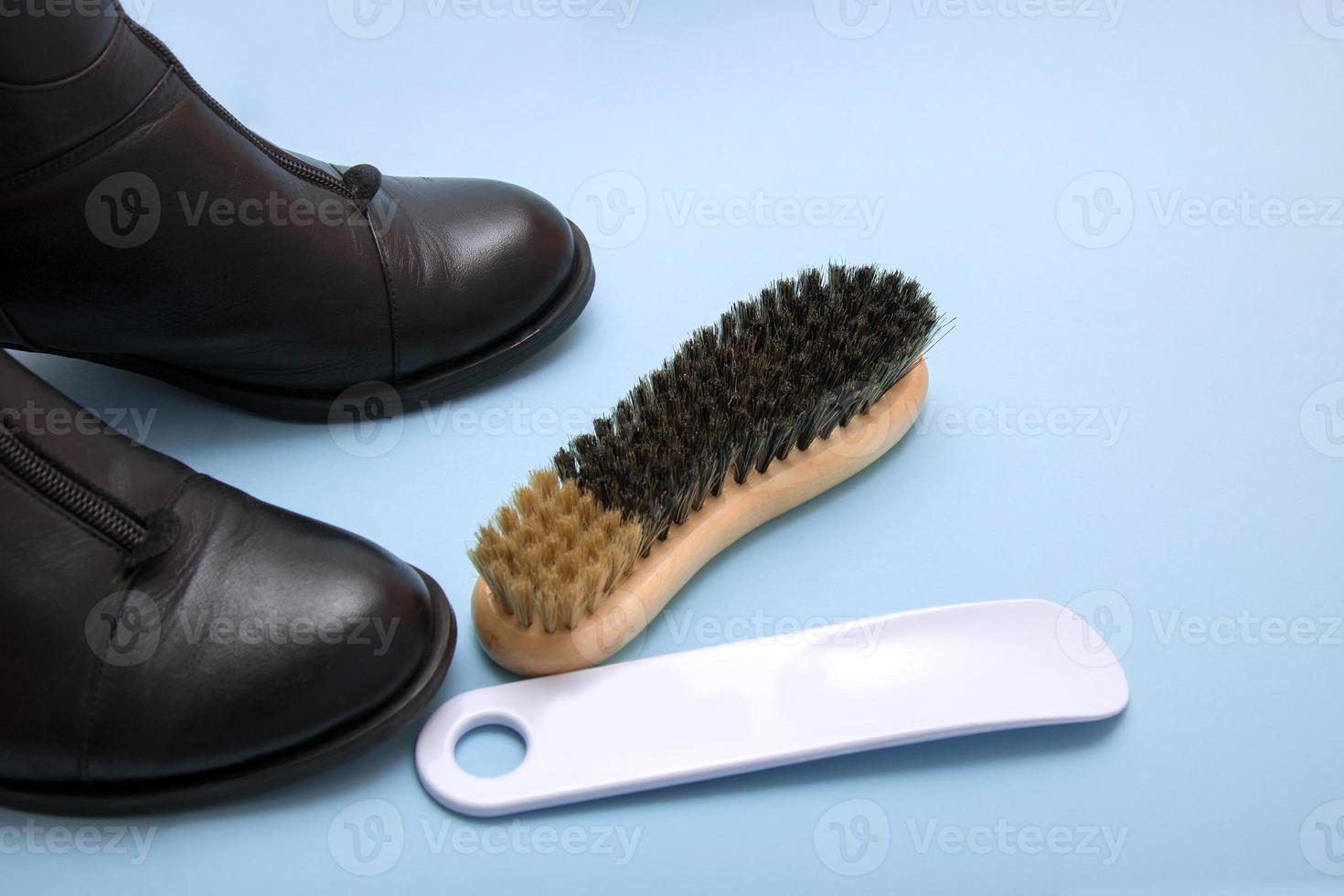 Schwarze Stiefel mit einem Schuhlöffel und einer Bürste auf blauem Grund foto