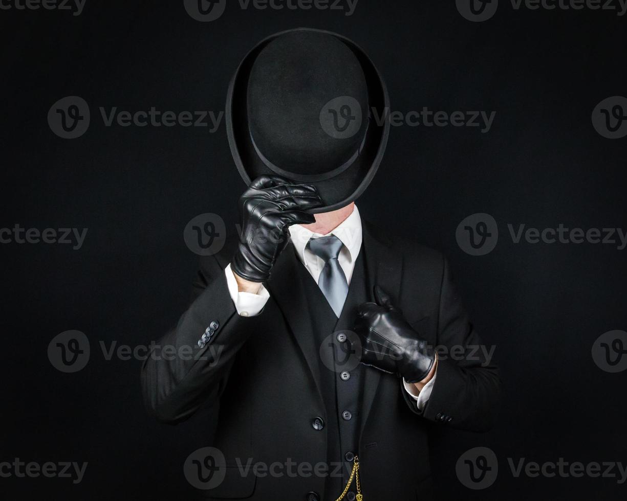 Porträt eines englischen Gentleman in dunklem Anzug und Lederhandschuhen, der zur Begrüßung Melone kippt. klassischer britischer butler oder geschäftsmann. foto