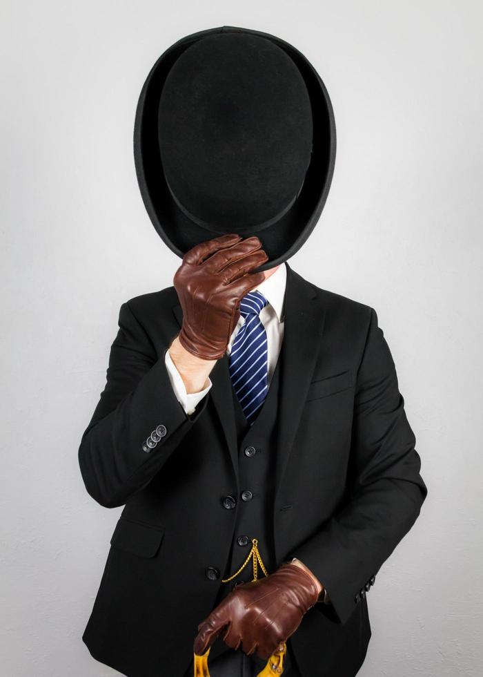 Porträt eines britischen Geschäftsmannes in dunklem Anzug und Regenschirm, der höflich Melone abnimmt. klassische Manieren des englischen Gentleman. foto