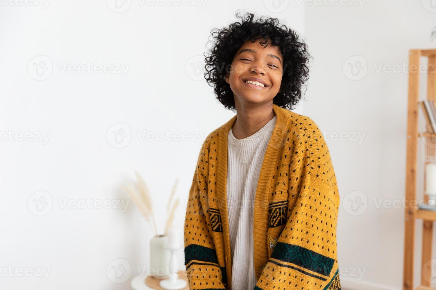 schönes afroamerikanisches mädchen mit afrofrisur, das zu hause drinnen lächelt. junge afrikanische frau mit lockigem haar, die im wohnzimmer lacht. freiheit glück sorglos glückliche menschen konzept. foto