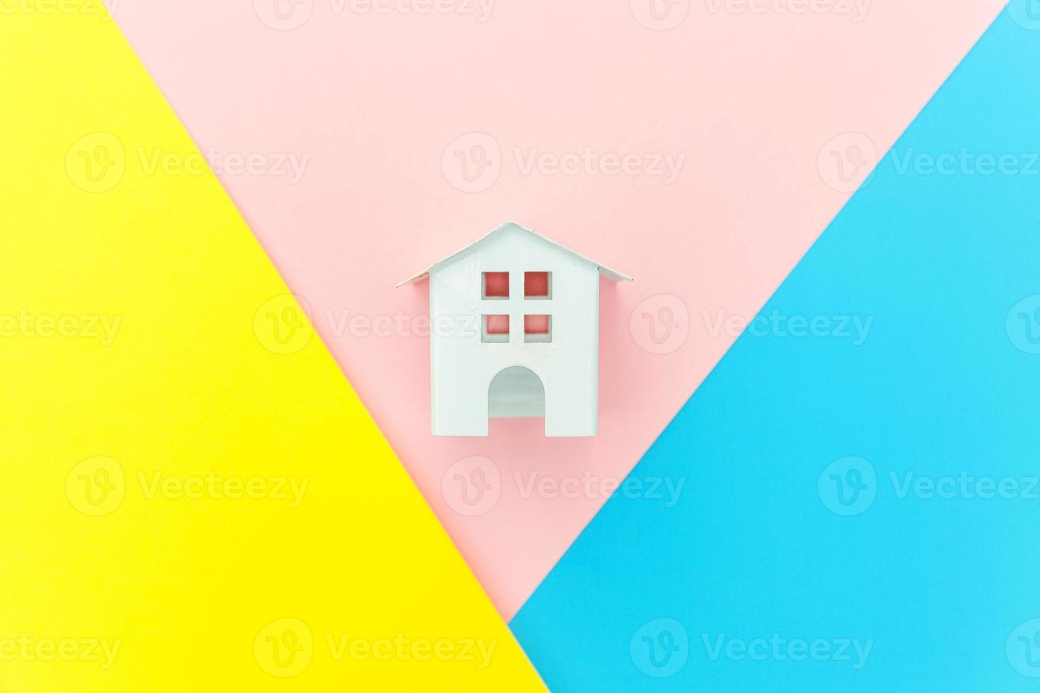 einfach design mit miniatur-weißem spielzeughaus isoliert auf blau gelb rosa pastell bunt trendy geometrischen hintergrund hypotheken-sachversicherung traumhaus konzept. flach liegend draufsicht kopierraum. foto