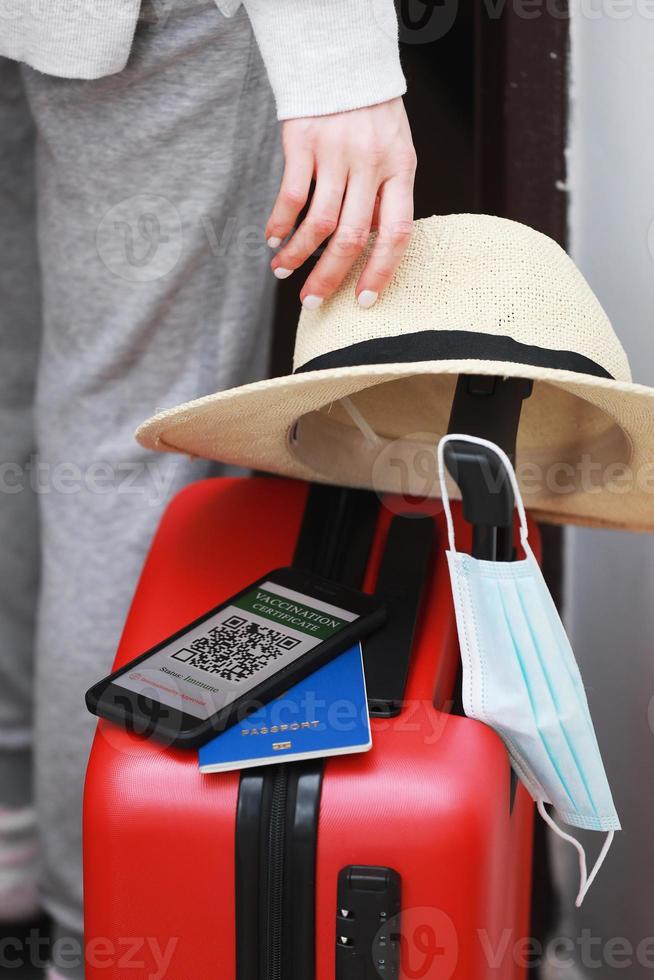 neues normales Konzept. Reisebereite Frau mit Smartphone mit einem digitalen Immun-Gesundheitspass. Frau mit Schutzmaske, Strohhut und Reisepass reist während einer Pandemie mit dem Flugzeug. foto