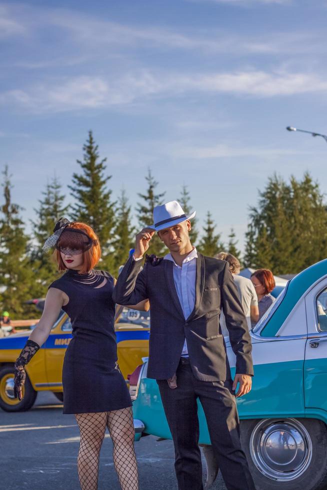 2022-08-12 Tatarstan, Bezirk Werchneuslonski, Dorf Savino. Erholungsort Swiyazhsky Hills. Kasaner Festival historischer Autos. Ein Mann und eine Frau in Retro-Kleidung posieren in der Nähe von Autos. foto