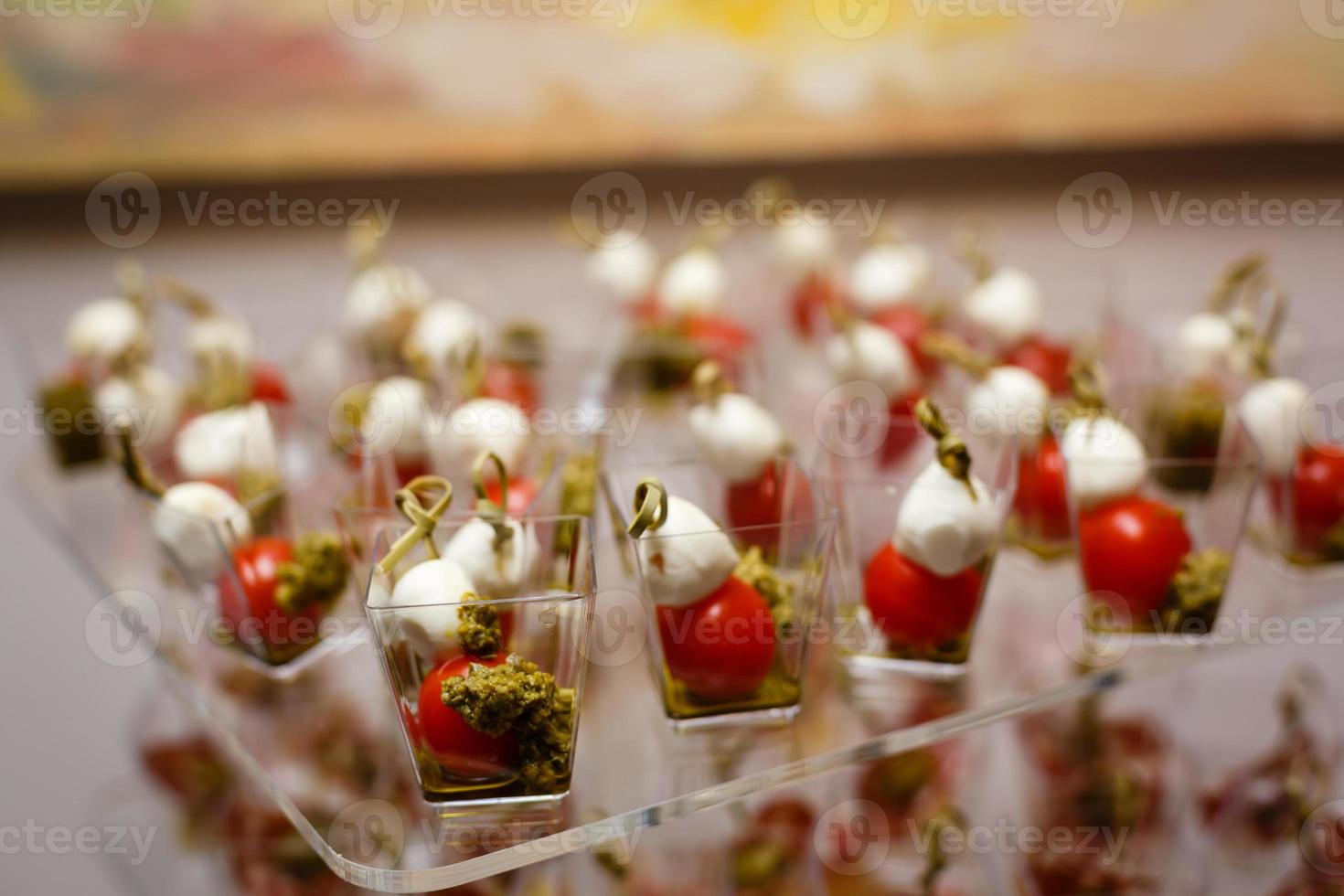 Catering für Partys. nahaufnahme von vorspeisen mit kirschtomaten, grünen oliven, olivenöl, käse und gewürzen in kurzen gläsern auf holzbraunem tisch. foto