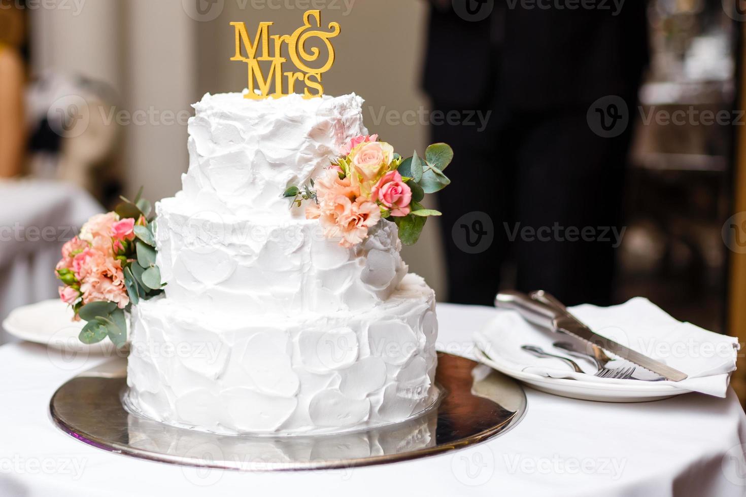 eine mehrstöckige weiße Hochzeitstorte auf einem silbernen Boden und rosa Blumen darauf foto