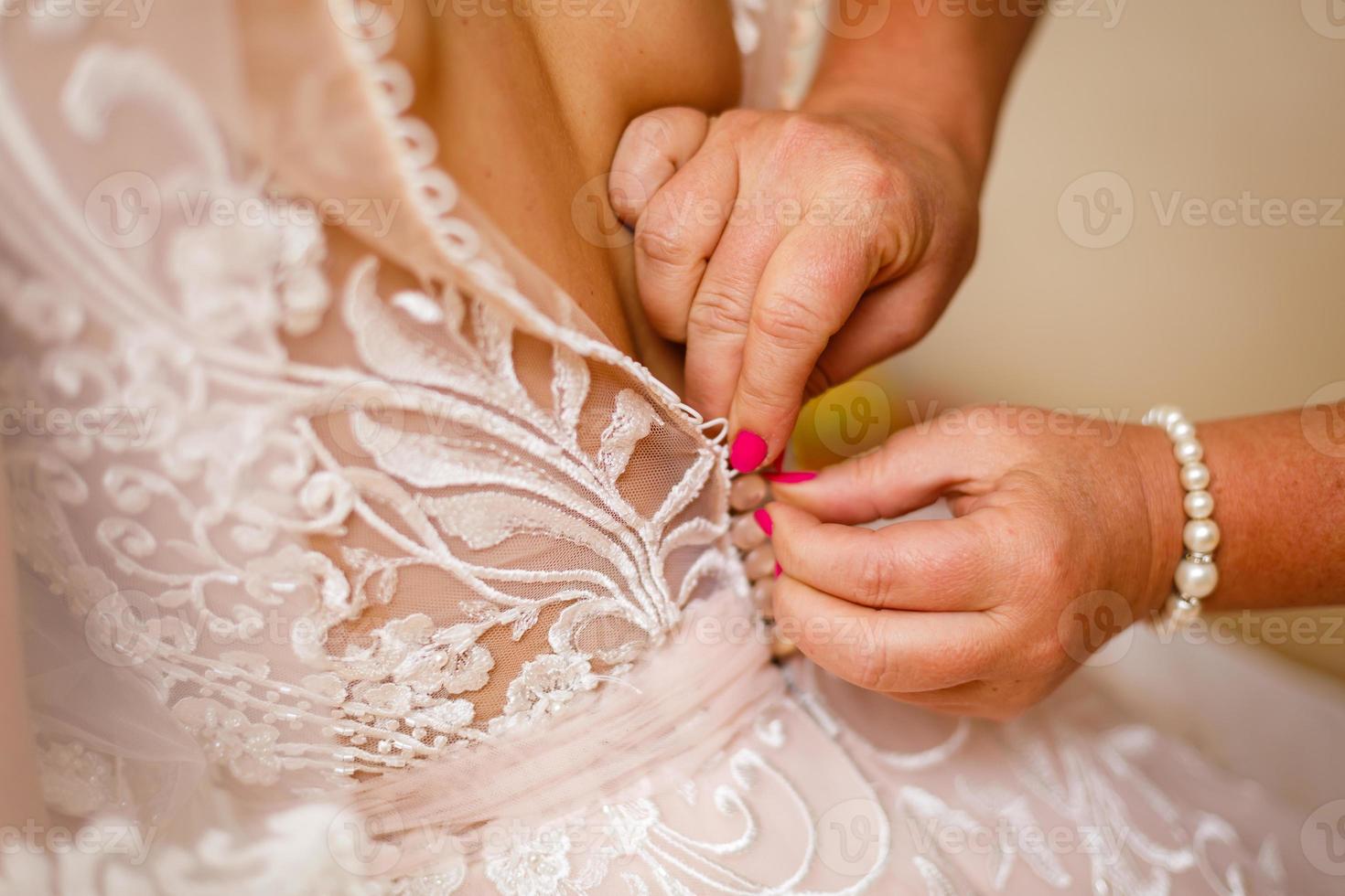 Die Hand der Freundin umklammert Knöpfe am Korsett der Braut foto