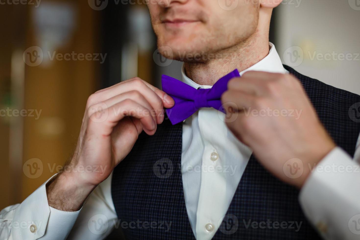 Schmetterling der violetten Farbe auf dem Hals beim Mann. Mann trägt lila, lila Fliege. Der Bräutigam geht zur Hochzeit. Hochzeitsmorgen. der mann richtet seine krawatte. foto