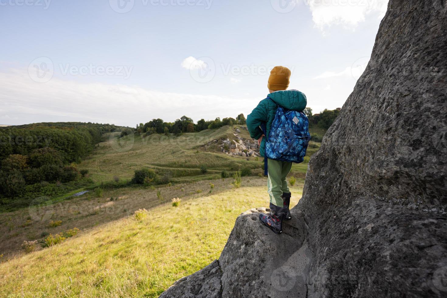 junge mit rucksack, der großen stein im hügel klettert. pidkamin, ukraine. foto
