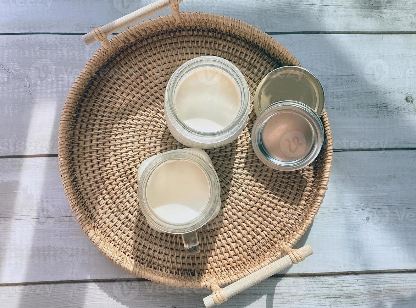 2 zwei Gläser Einmachgläser mit natürlichem hausgemachtem Naturjoghurt, Joghurt, auf dem handgewebten Rattantablett, Weidenkorb in abgerundeter Form, Hochwinkelansicht. weiche Themenfarbe im koreanischen Café-Stil foto