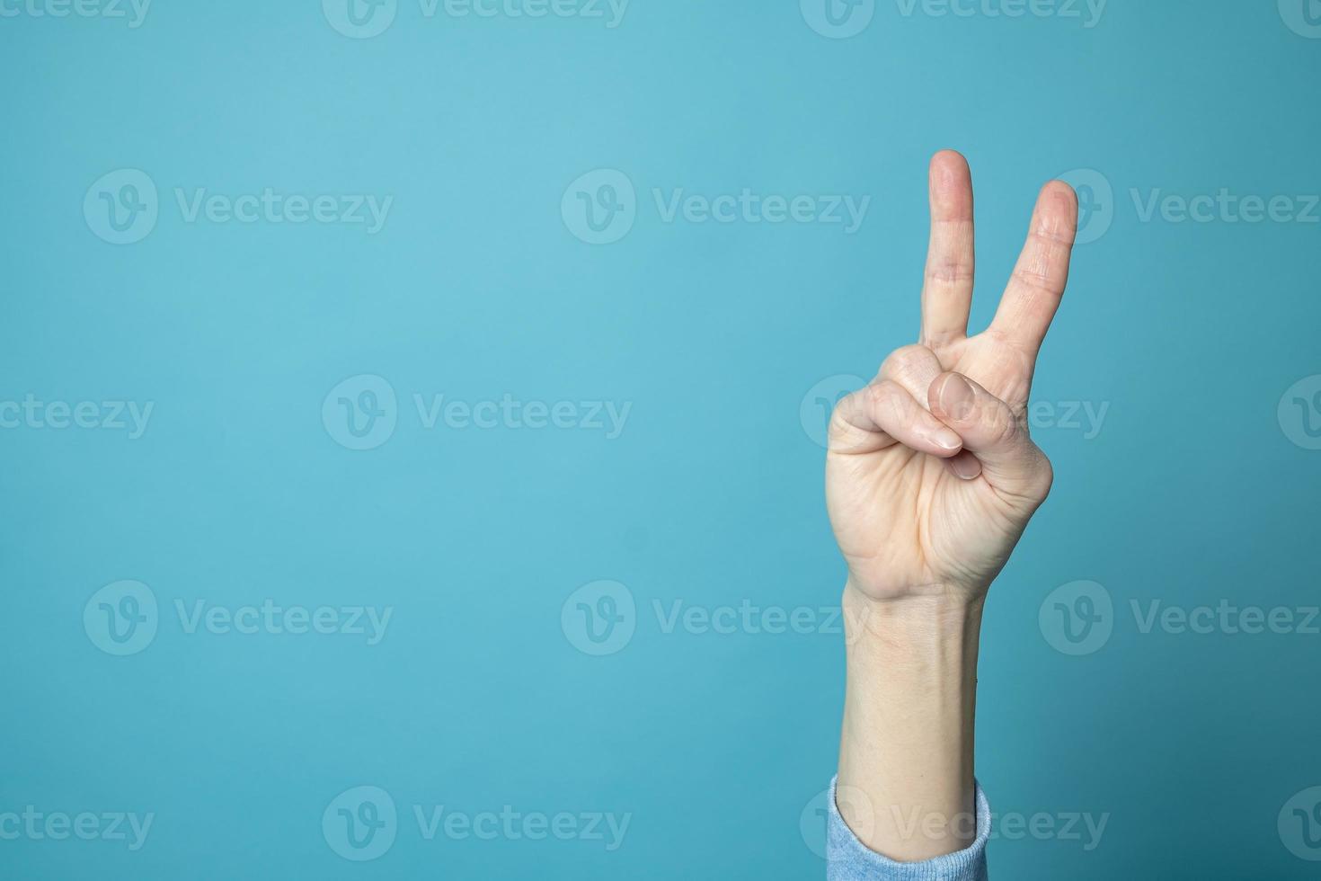 Victory-Zeichen, zwei Finger hoch, auf blauem Hintergrund. Platz kopieren. foto