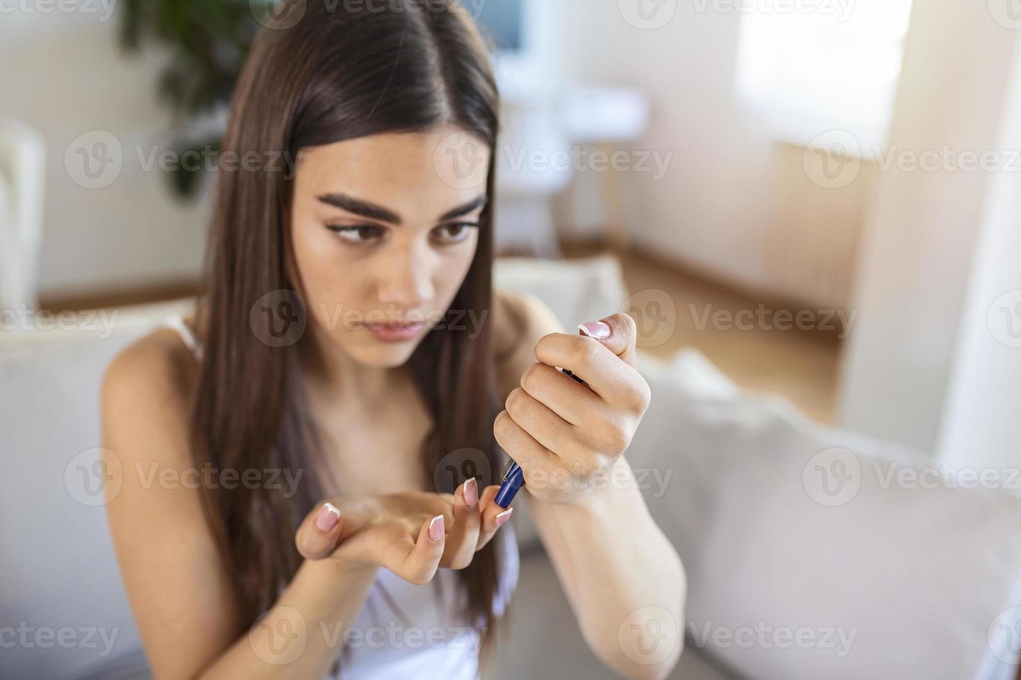 Frau mit Lanzette am Finger. Frau macht Blutzuckertest zu Hause in einem Wohnzimmer. Diabeteskontrolle foto