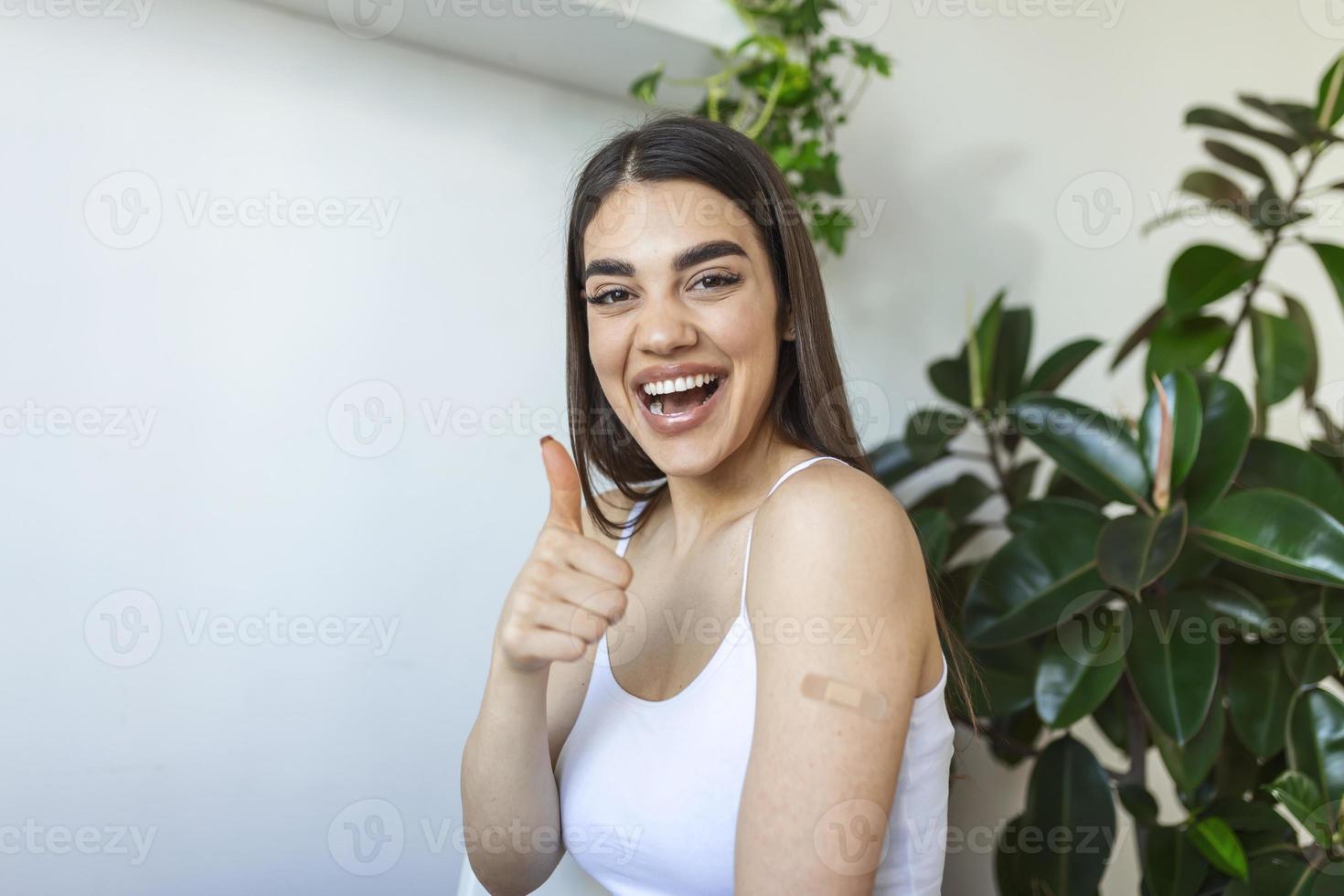 geimpfte junge Frau, die mit dem Daumen nach oben gestikuliert, um die Impfung zu genehmigen, häuslicher Hintergrund foto