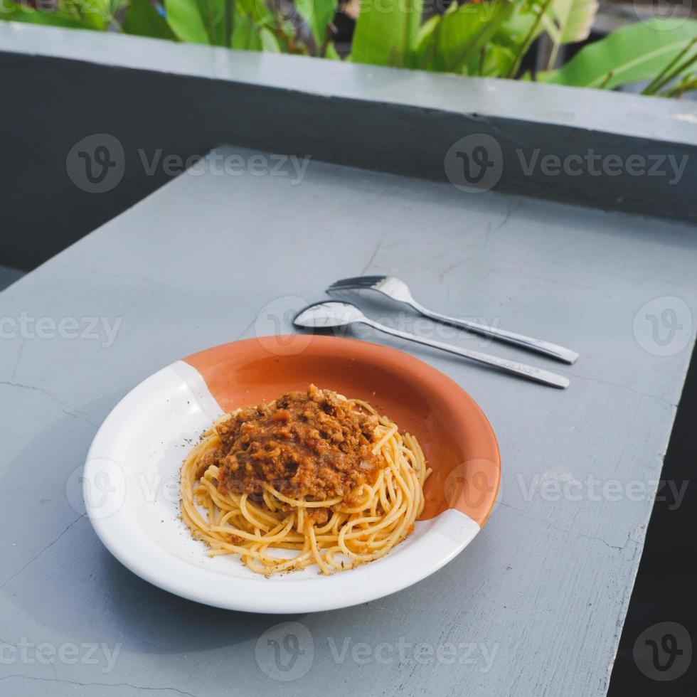 Gesunder Teller mit italienischen Spaghetti, gekrönt mit einer leckeren Bolognese-Sauce aus Tomaten und Rinderhackfleisch und frischem Basilikum auf einem grauen Tisch. mit Cappuccino serviert foto