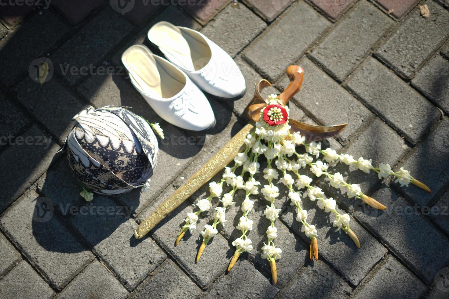 ein paar schuhe, kopfschmuck und kris oder zeremonieller dolch mit jasmin- und magnolienblumenhalskette für eine traditionelle hochzeitszeremonie in indonesien foto